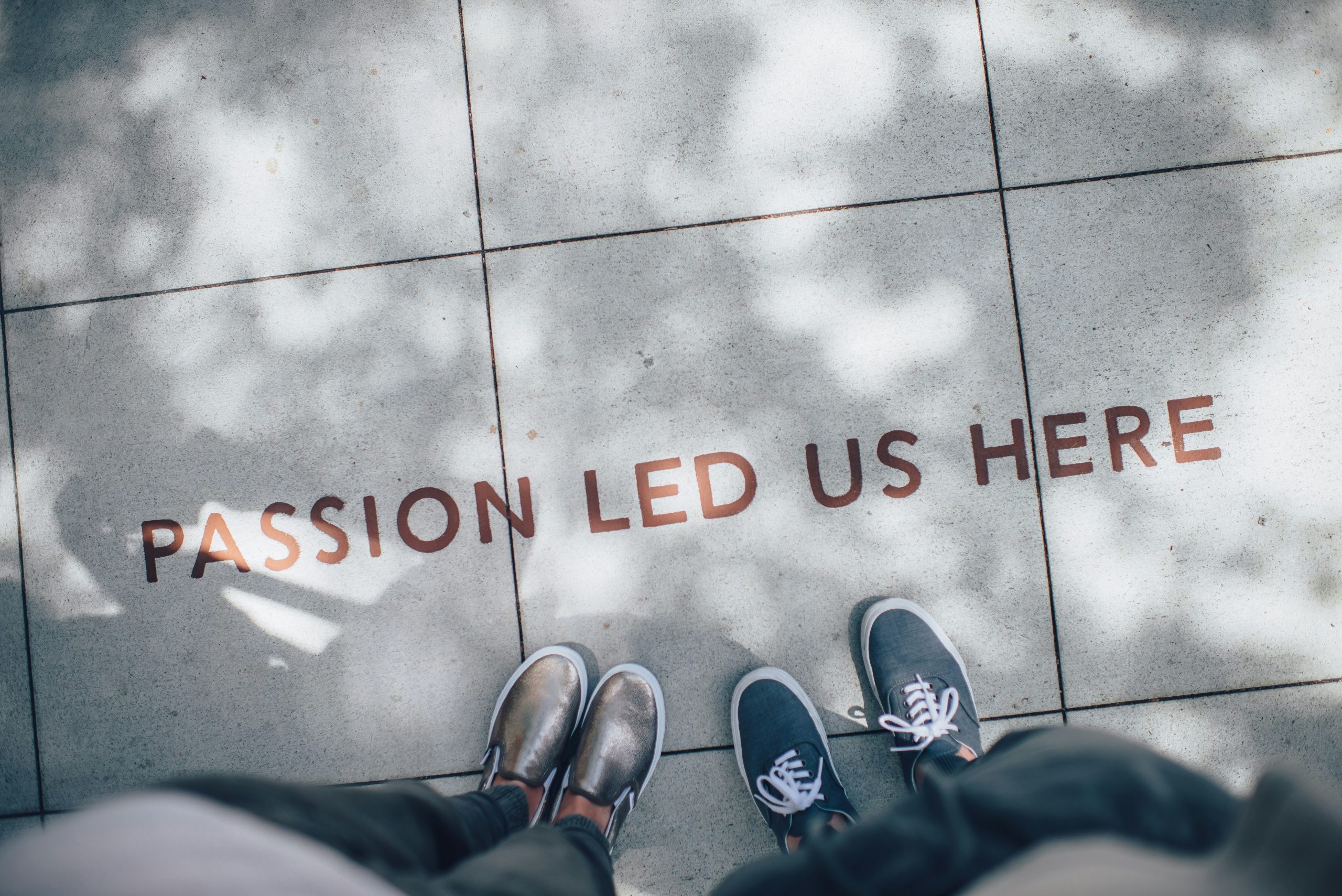 Image of feet on a sidewalk facing the words, "PASSION LED US HERE"<br />
